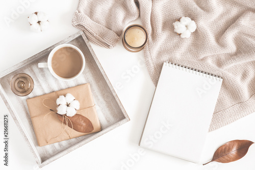 Autumn or winter composition. Cup of coffee, gift, dried autumn leaves, beige sweater, notepad on white background. Flat lay, top view, copy space