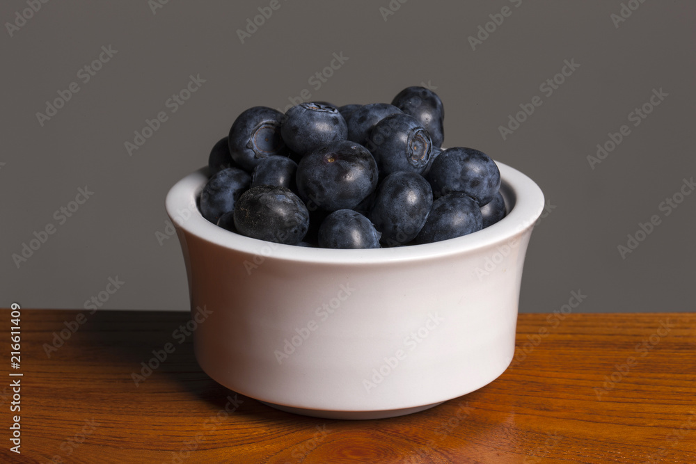 blue barry on the white ceramic, wood table, grey background. blue barry on the white ceramic, wood table, grey background.