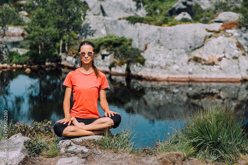 Young girl in pink T-shirt and black leggings sitting on a stone in lotus pose near the lake. concept of yoga, pilates, healthy life.