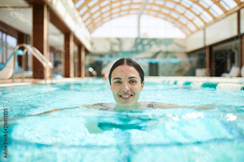 Young smiling swimmer with her head over water looking at you while enjoying vacation at spa resort
