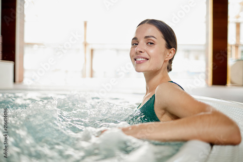 Young woman relaxing in soft waving water while sitting in jacuzzi bath at spa center
