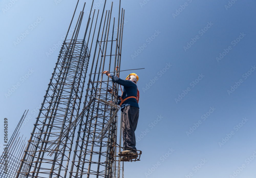 worker at altitude strengthens the pillars from rebar, on the blue sky background. candid, real people worker at altitude strengthens the pillars from rebar, on the blue sky background. candid, real people
