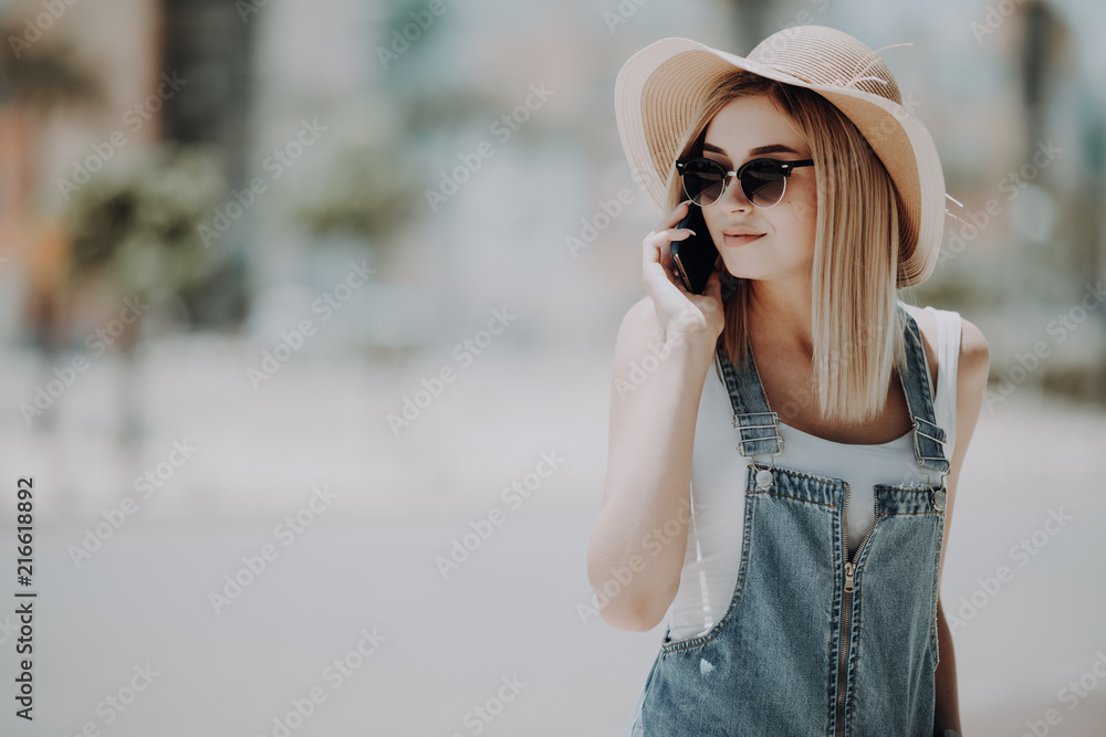 Hello from summer. Young pretty tourist is talikg on the mobile, wearing sunglasses and hat, smiling Hello from summer. Young pretty tourist is talikg on the mobile, wearing sunglasses and hat, smiling