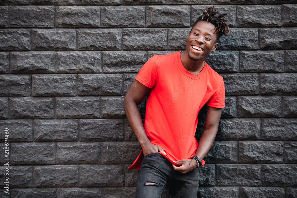 African smiling male model standing in empty red t-shirt against brick wall African smiling male model standing in empty red t-shirt against brick wall