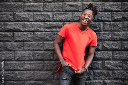African smiling male model standing in empty red t-shirt against brick wall