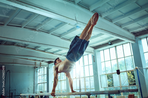The sportsman performing difficult gymnastic exercise at gym. The sport, exercise, gymnast, health, training, athlete concept. Caucasian fit model