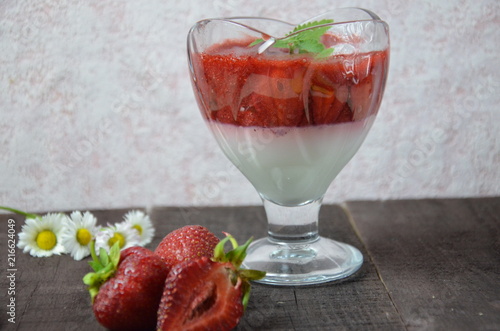 Summer dessert, panna cotta or yogurt or pudding or jam with strawberrieswith strawberries decorated with mint leaves. On a brown wooden table, bright sunlight. Copy space. close up photo