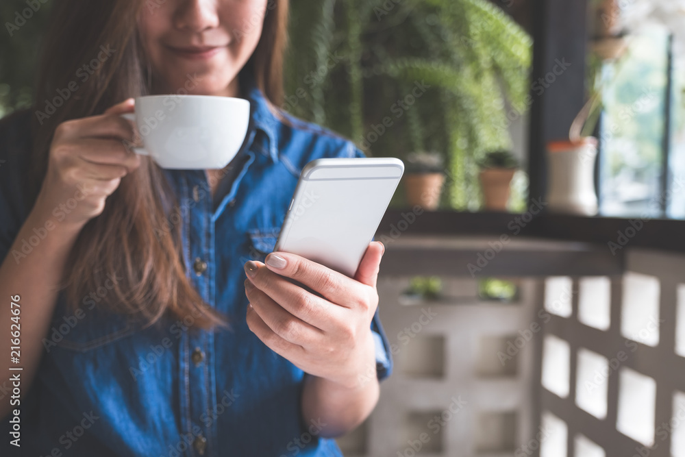 Closeup image of a woman holding , using and touching a smart phone while drinking coffee Closeup image of a woman holding , using and touching a smart phone while drinking coffee