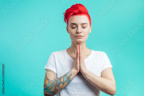 girl holding hands together and doing yoga. namaste position. free time. woman practising yoga. meditation with closed eyes. hipster is trying to calm down. copy space. isolated blue background photo