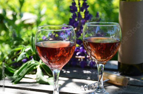 Red wine poured into wine glass on background of green tree leaf foliage. purple flower