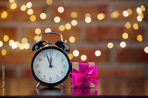 handmade gift box with purple bow and alarm clock on wooden table with fairy lights on bokeh background