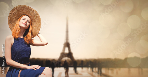 Young girl in dress and hat sitting at street with Parisian Eiffel tower on background. Image with bokeh and in vintage style