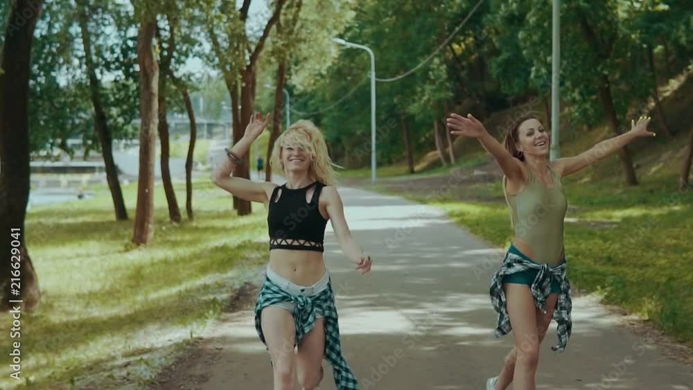 Young hipster womans in shorts with shirts runs in park. Young girls have fun outdoors in slow motion. Party concept Young hipster womans in shorts with shirts runs in park. Young girls have fun outdoors in slow motion. Party concept