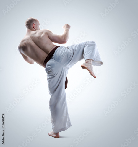 Karate man in a kimono demonstrate pose on a gray background. Studio shoot.