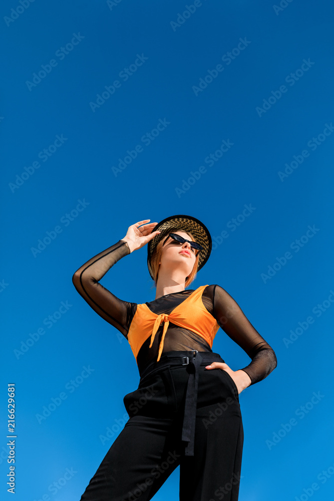 bottom view of girl posing in trendy sunglasses and stylish hat, blue sky on background bottom view of girl posing in trendy sunglasses and stylish hat, blue sky on background