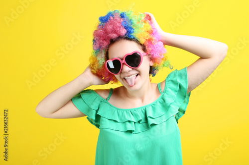 Young girl in clown wig and sunglasses on yellow background