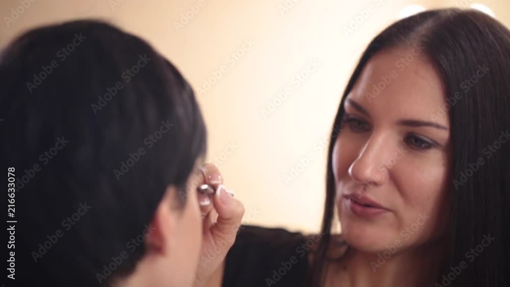 The make-up artist communicates and colors the eyes of the model. View from the back The make-up artist communicates and colors the eyes of the model. View from the back