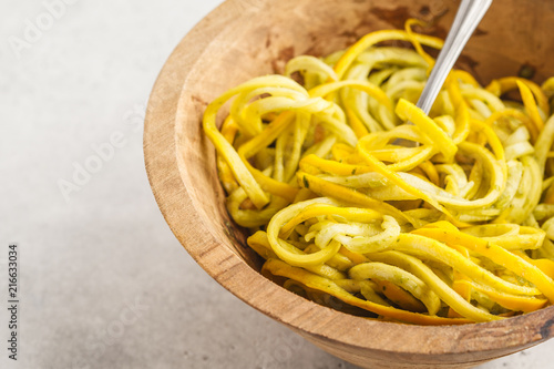 Raw vegan zucchini noodles in a wooden bowl, white background.