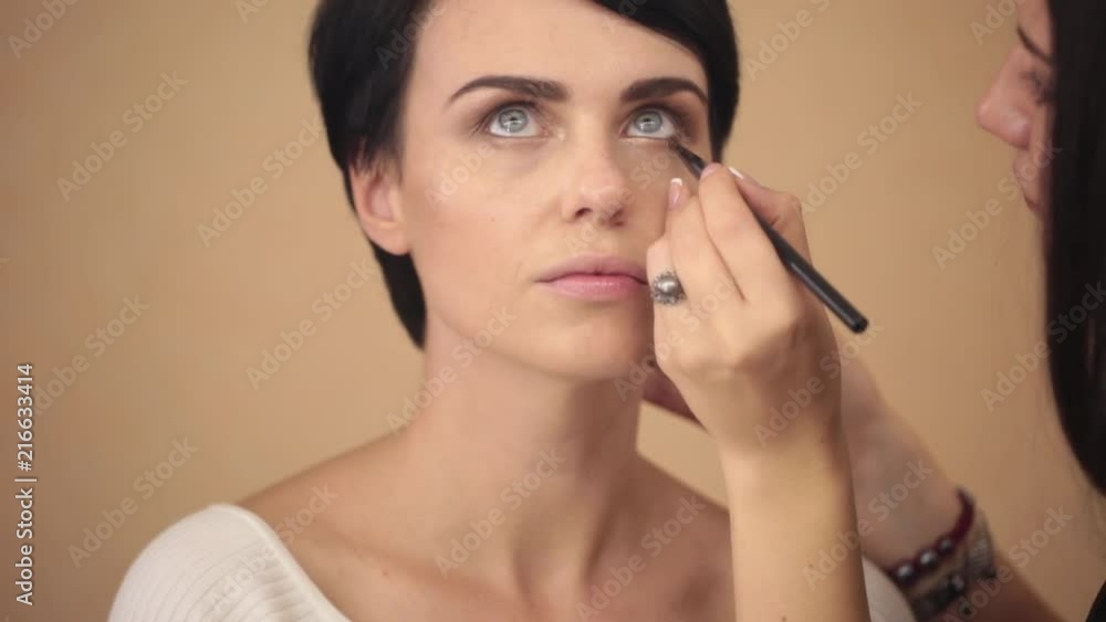The make-up artist paints the eyes of the model with a brush. The make-up artist paints the eyes of the model with a brush.