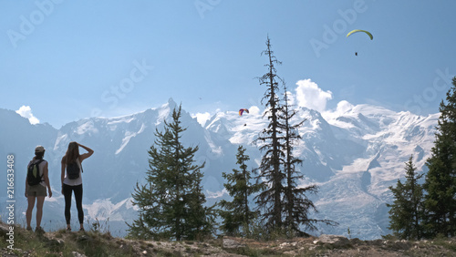 Females hikers enjoy the views of para gliders and the mountains over the valley of Chamonix, Ffrance and toward Mont Blanc in the french alps.