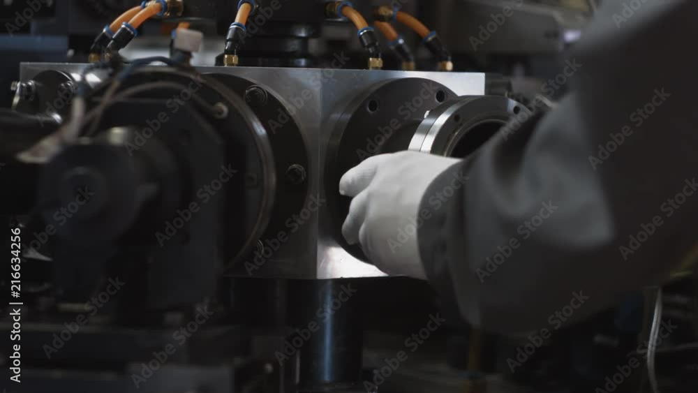 Unrecognizable engineer in gray uniform and gloves repairs modern production machine, replacing part of pneumatic transport mechanism. Factory or plant indoor. Close-up of hands. Unrecognizable engineer in gray uniform and gloves repairs modern production machine, replacing part of pneumatic transport mechanism. Factory or plant indoor. Close-up of hands.
