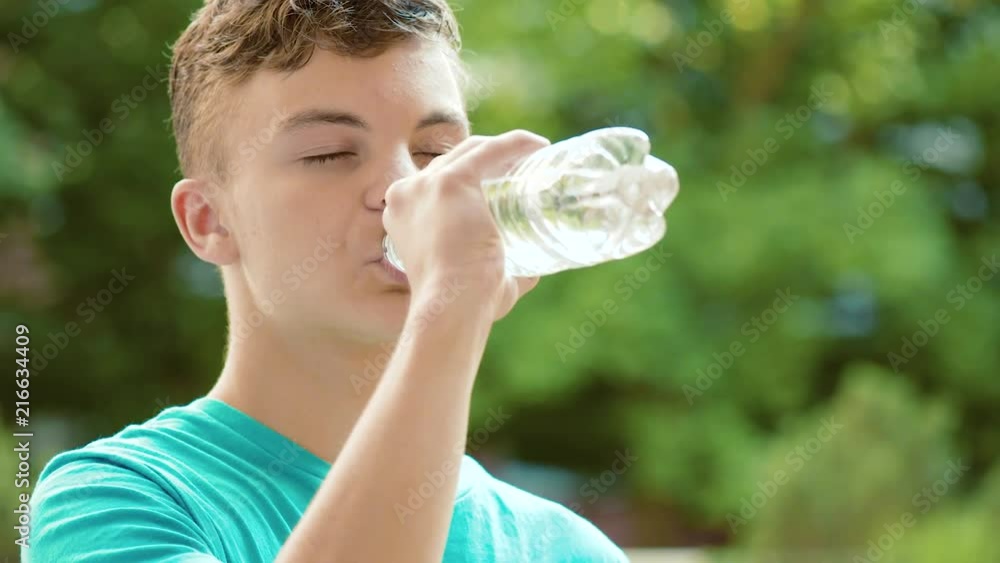 Happy teen boy drinking water from plastic bottle in summer park. Cute teenager drinks cold water - outdoors portrait. Happy teen boy drinking water from plastic bottle in summer park. Cute teenager drinks cold water - outdoors portrait.