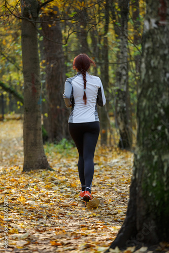 Photo from back of young brunette woman running through autumn park