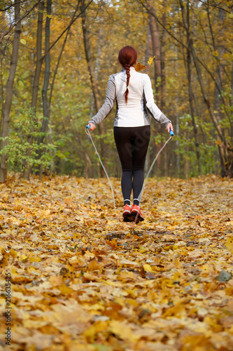 Photo from back of athlete woman jumping with rope at autumn forest © Sergey