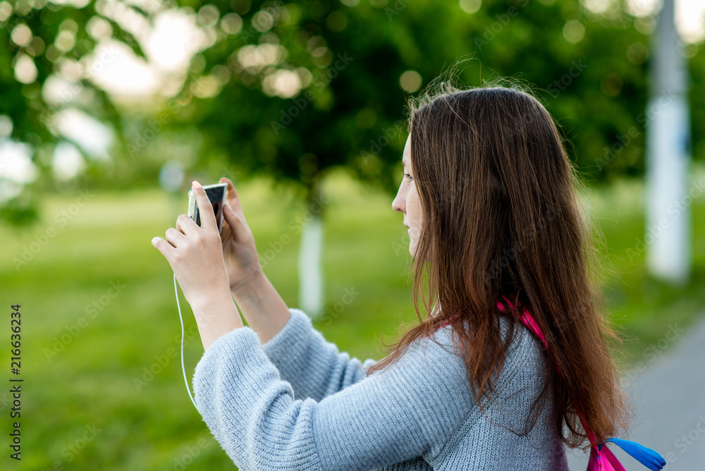 Girl schoolgirl in summer outdoors. In his hands holds a smartphone. Take pictures of the landscape on your phone. Photographs in city. Girl schoolgirl in summer outdoors. In his hands holds a smartphone. Take pictures of the landscape on your phone. Photographs in city.