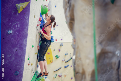 Photo of young woman with safety rope practicing on climbing wall