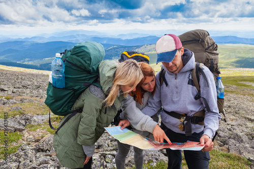 A team of travelers from two women and men with backpacks orient themselves to the terrain, study maps and navigate the route through the mountains. 