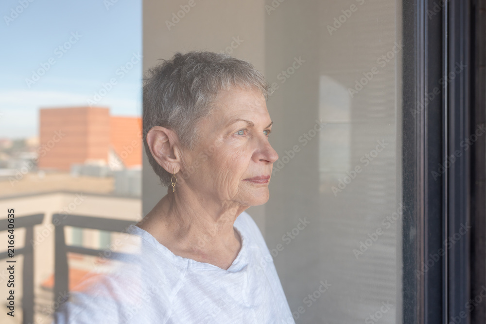 Close up of older woman with short grey hair and white top seen through glass sliding door (selective focus) Close up of older woman with short grey hair and white top seen through glass sliding door (selective focus)