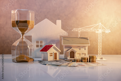 Real estate or property development. Construction business investment concept. Home mortgage loan rate. Coin stack on international banknotes with hourglasses, house and crane models on the table. photo