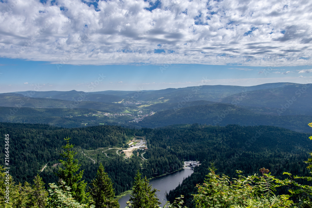 View from a top of a mountain in the valley with a lake and clouds on the sky in the bavarian forest