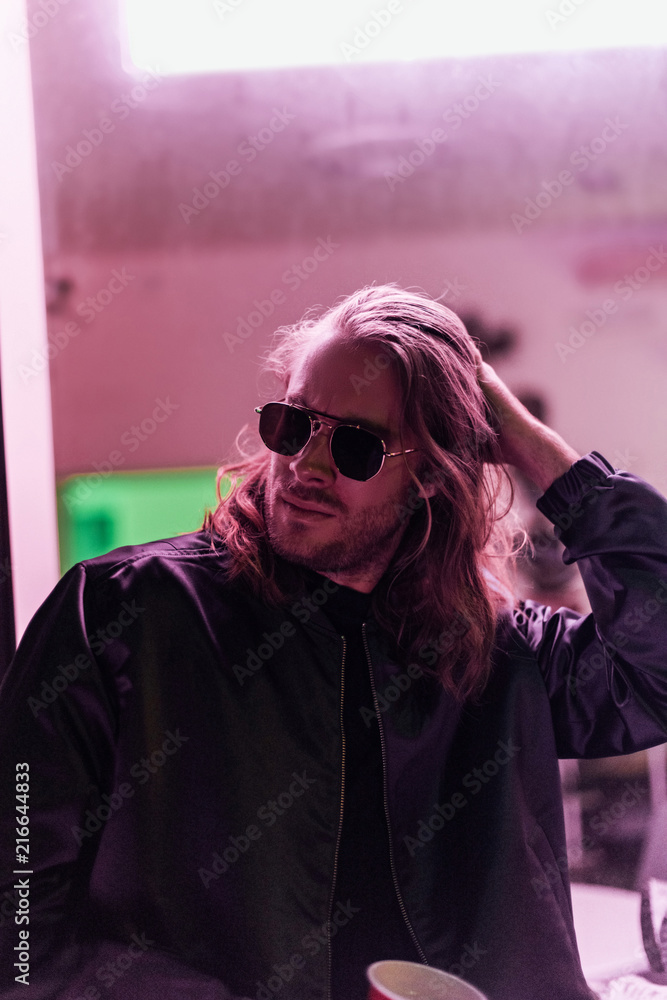 handsome young man in leather jacket and sunglasses spending time on street at night under pink light handsome young man in leather jacket and sunglasses spending time on street at night under pink light