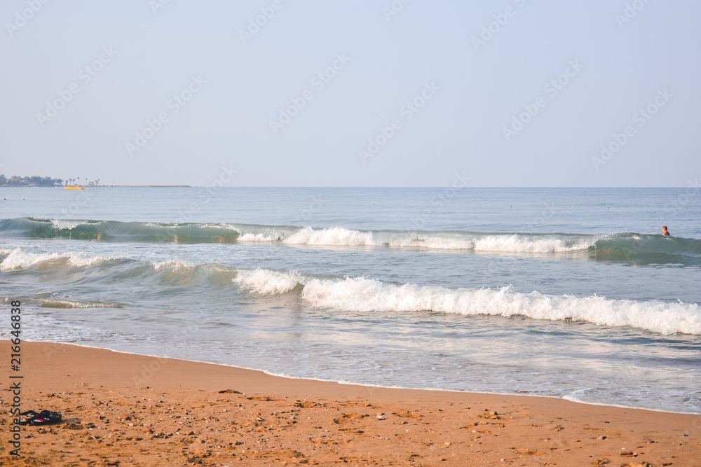 The sea sandy beach in the early morning, on the sea, among the waves, a man is bathing.