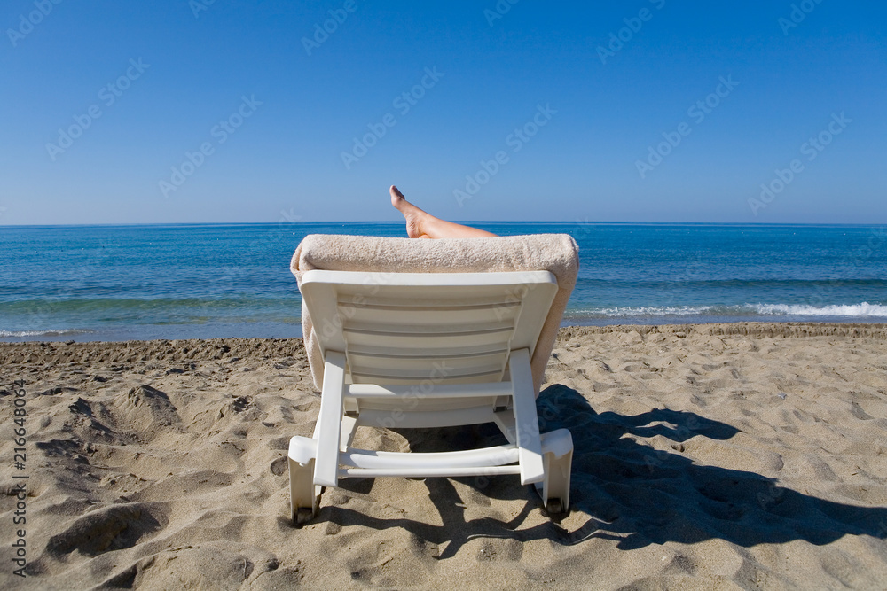 A man is resting on a deckchair by the sea.