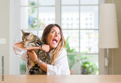 Young woman at home playing with her cat annoyed and frustrated shouting with anger, crazy and yelling with raised hand, anger concept photo