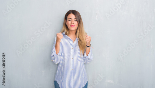 Young adult woman over grey grunge wall wearing fashion business outfit excited for success with arms raised celebrating victory smiling. Winner concept. © Krakenimages.com