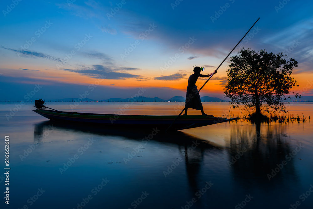 Silhouette fisherman on boat over the lake with sunrise and dramatic sky