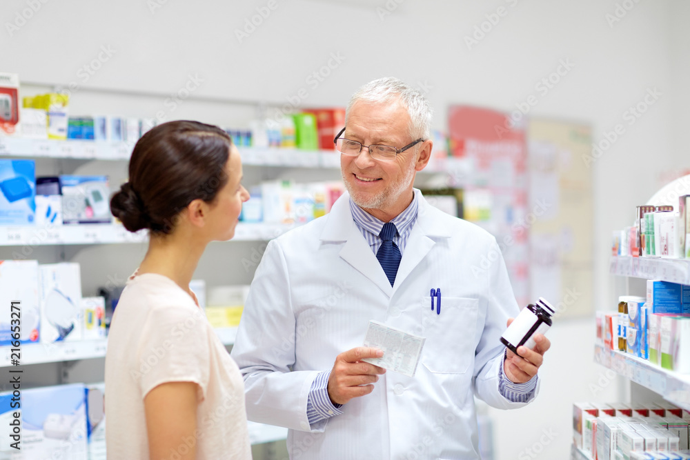 Obraz premium medicine, healthcare and people concept - senior apothecary with drugs and female customer at pharmacy