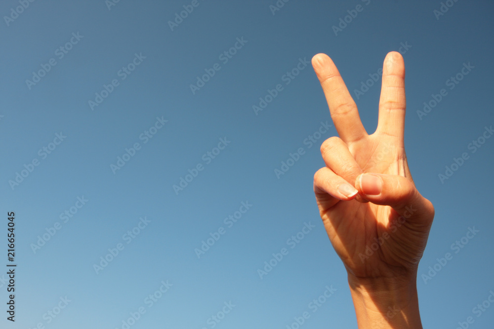 woman raising two fingers up on hand it is shows peace strength fight or victory symbol and letter V in sign language on sky. woman raising two fingers up on hand it is shows peace strength fight or victory symbol and letter V in sign language on sky.