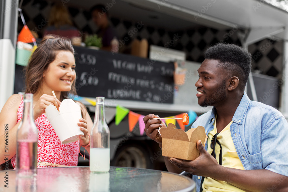 leisure and people concept - happy mixed race couple eating and talking at food truck leisure and people concept - happy mixed race couple eating and talking at food truck