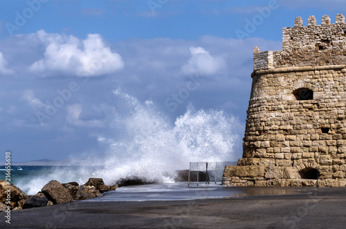 Heraklion, Crete Island - Greece. Sea waves hitting the breakwaters next to the Venetian fortress Koules at the old port of Heraklion city. Sunny day with blue cloudy sky