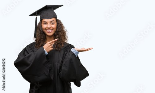 Young hispanic woman wearing graduation uniform very happy pointing with hand and finger