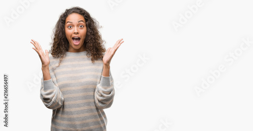 Beautiful young hispanic woman wearing stripes sweater celebrating crazy and amazed for success with arms raised and open eyes screaming excited. Winner concept © Krakenimages.com