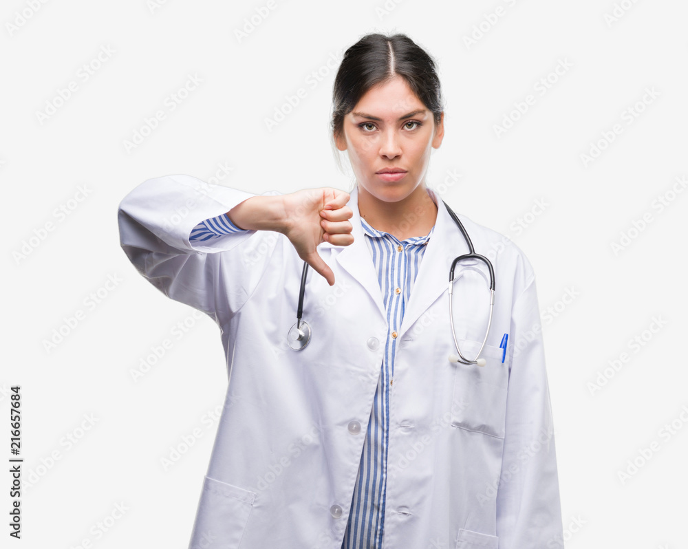 Young hispanic doctor woman with angry face, negative sign showing dislike with thumbs down, rejection concept Young hispanic doctor woman with angry face, negative sign showing dislike with thumbs down, rejection concept
