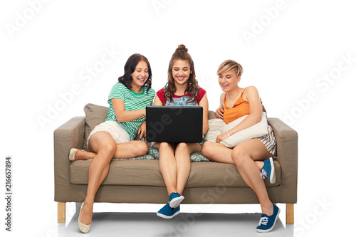 friendship, leisure and technology concept - group of happy smiling female friends with laptop computer sitting on sofa over white background