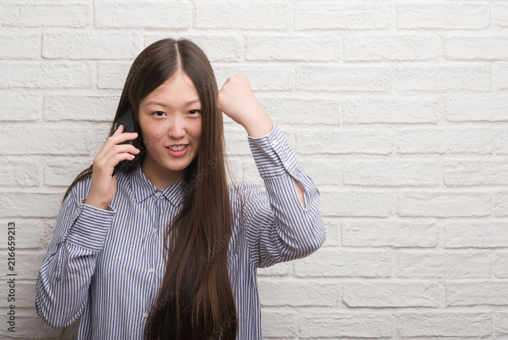 Young Chinese woman over brick wall talking on the phone annoyed and frustrated shouting with anger, crazy and yelling with raised hand, anger concept Young Chinese woman over brick wall talking on the phone annoyed and frustrated shouting with anger, crazy and yelling with raised hand, anger concept