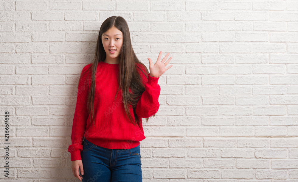 Young Chinese woman over brick wall showing and pointing up with fingers number five while smiling confident and happy. Young Chinese woman over brick wall showing and pointing up with fingers number five while smiling confident and happy.